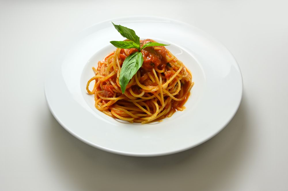 Spaghetti with tomato sauce and fresh basil on a white plate