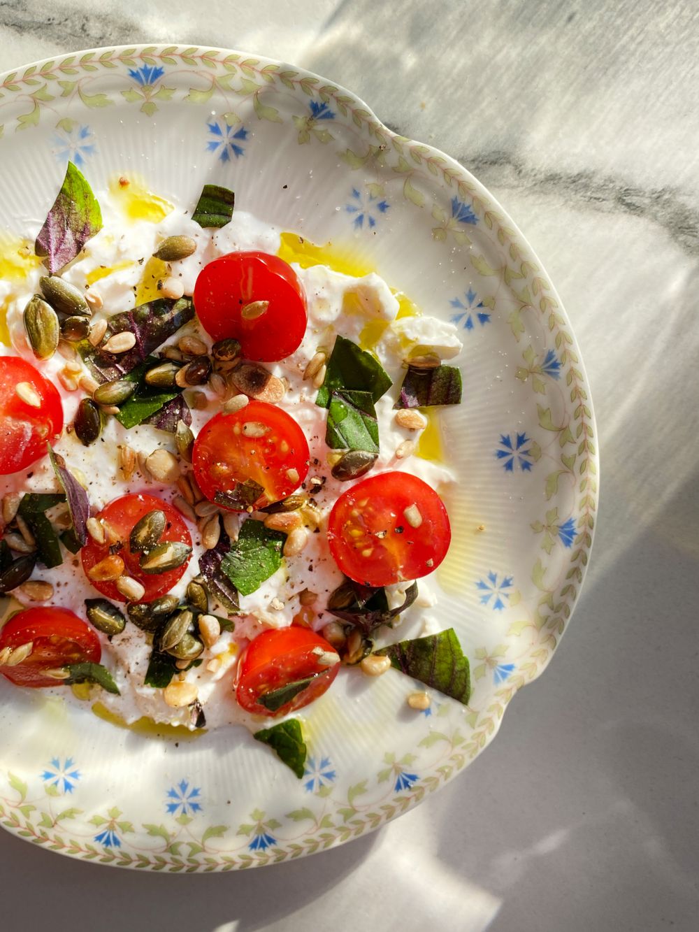 Burrata with cherry tomatoes, basil, and olive oil on a blue-and-white floral plate